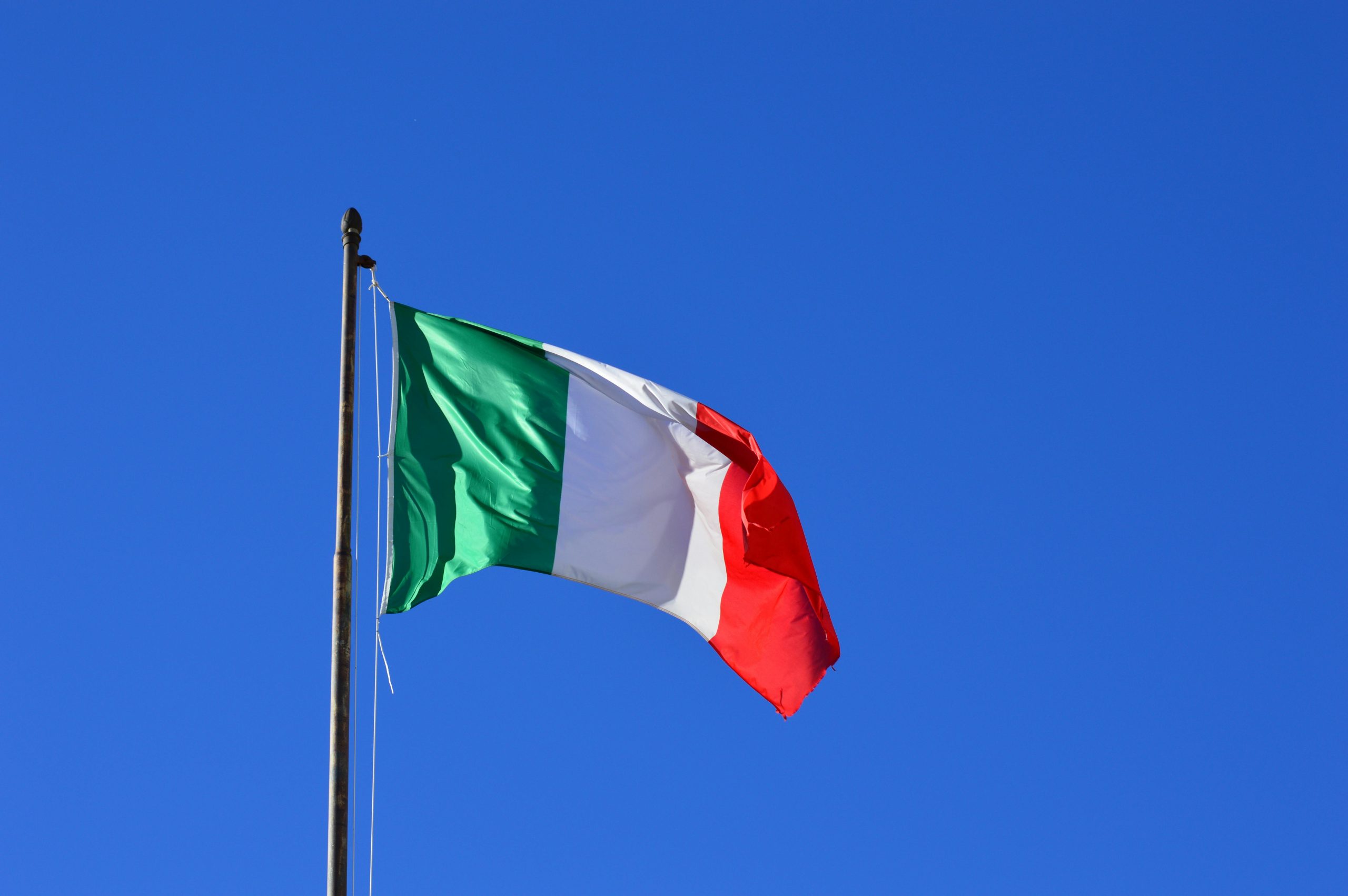 Italian flag flying against a vibrant blue sky, symbolizing national pride and identity.