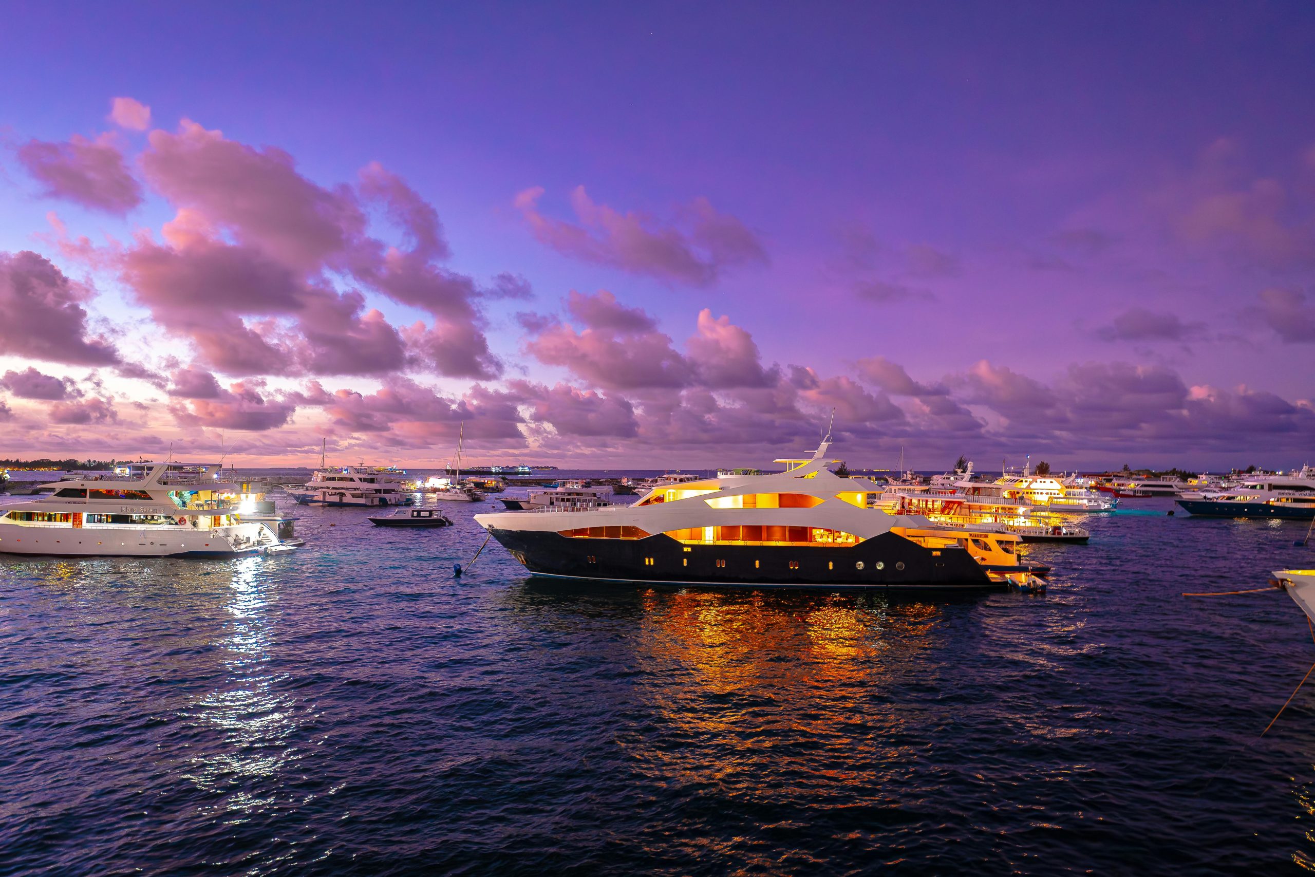 A scenic view of luxury yachts illuminated at sunset in the Maldives, offering a serene travel experience.